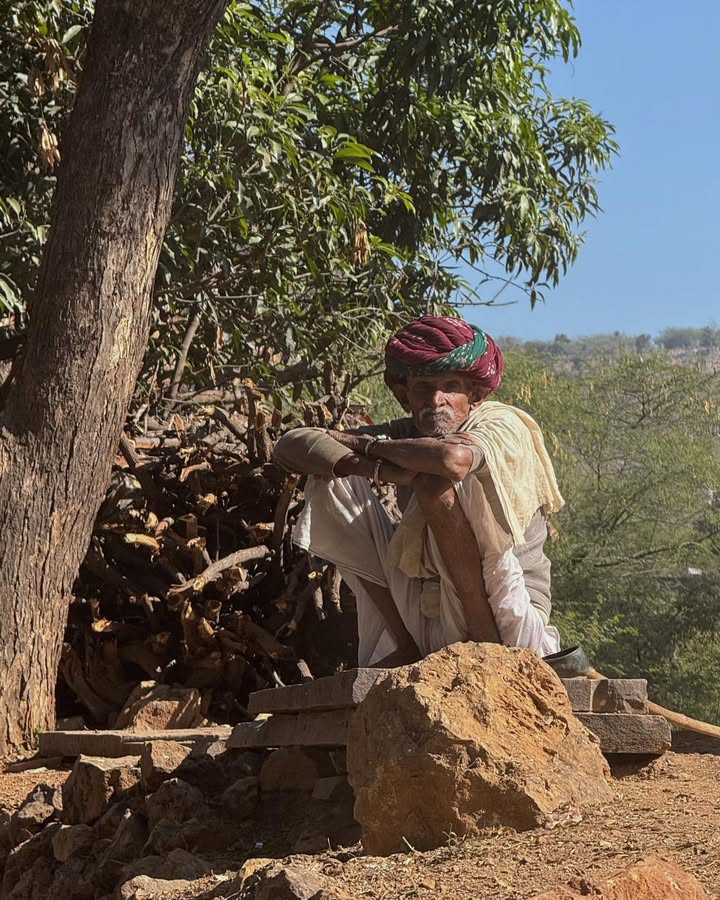 Under the quiet shade of a tree on a dusty countryside road,
I noticed a man sitting beside a pile of firewood.